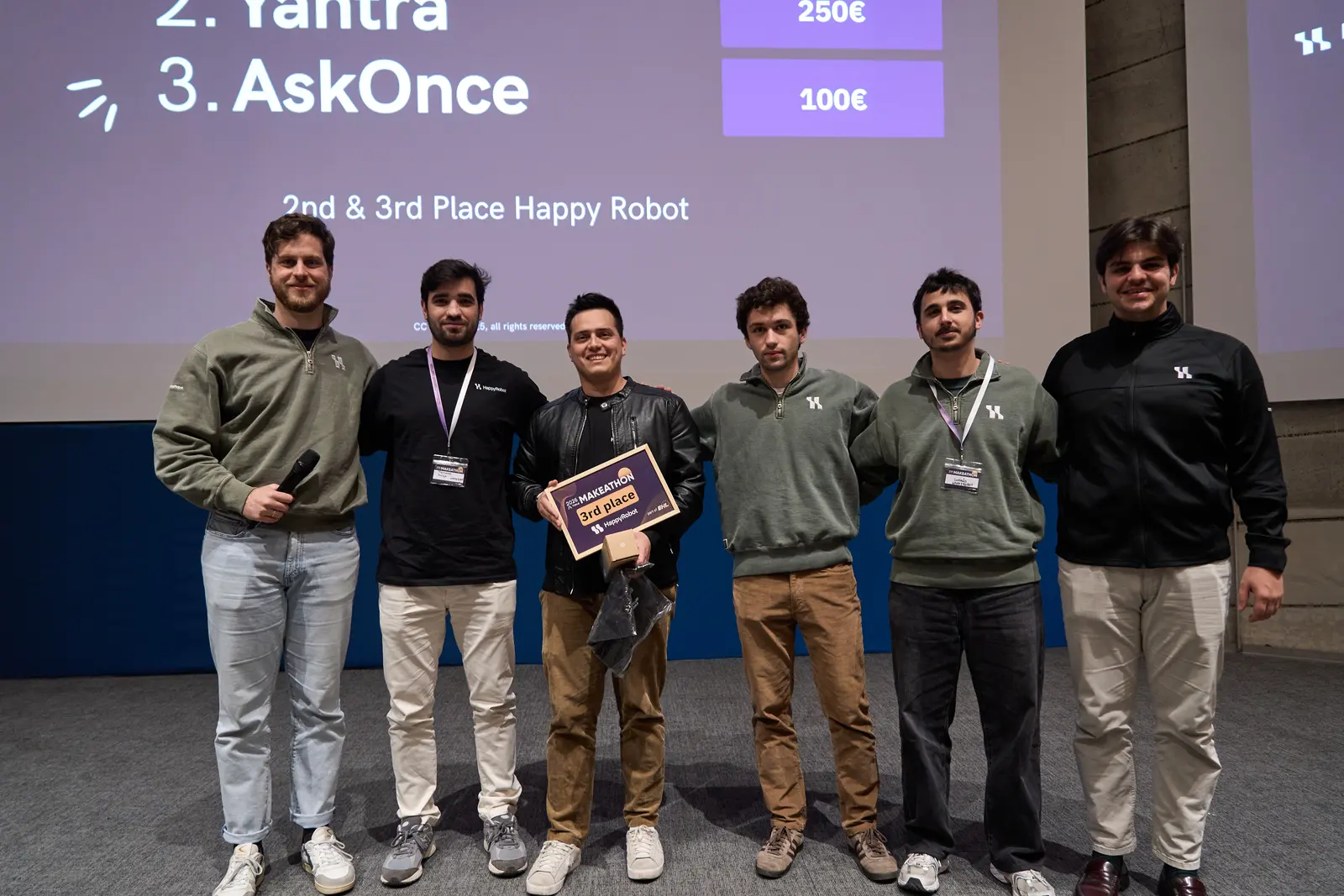 Javier sosteniendo la placa de 3er lugar en el escenario de la premiación del Makeathon